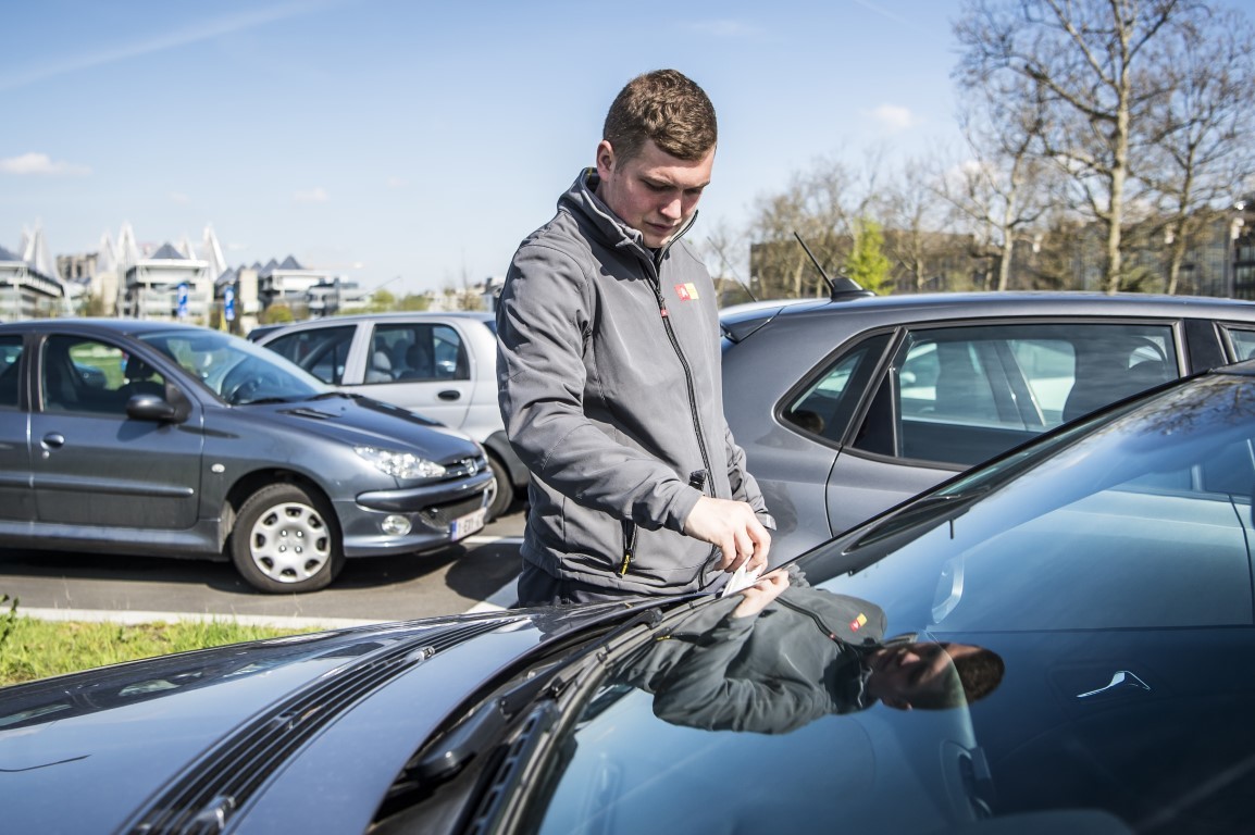 Parkeerwachter plaatst retributiebon achter de ruit van een voertuig Parkeerwachter plaatst retributiebon achter de ruit van een voertuig